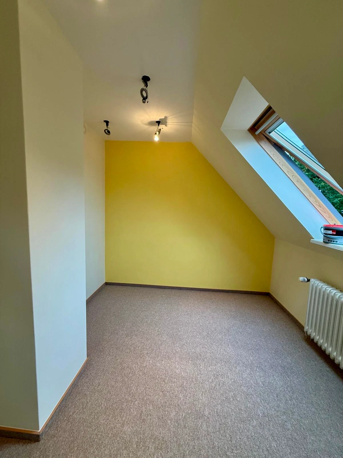 Dachzimmer mit gelb gestrichener Akzentwand zwischen weißen Schrägen