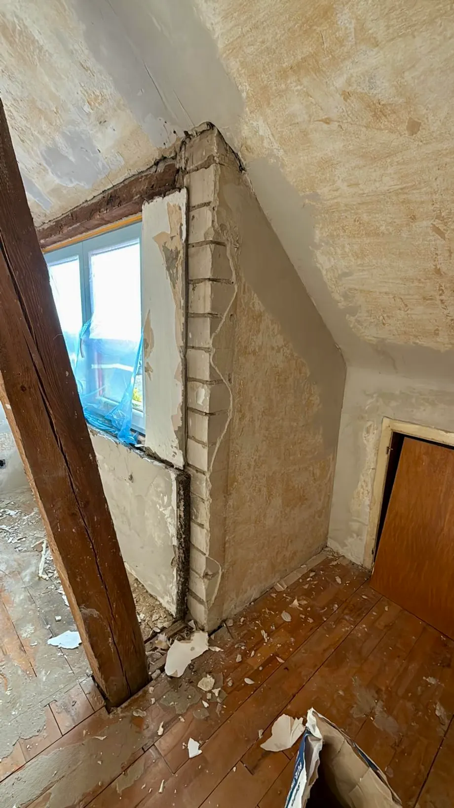 Dachzimmer im Rohbau: alter Putz an Decke und Fensterleibung, freiliegende Holzbalken