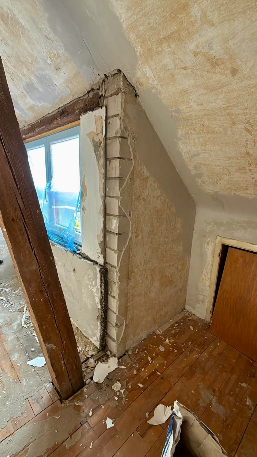 Dachzimmer im Rohbau: alter Putz an Decke und Fensterleibung, freiliegende Holzbalken